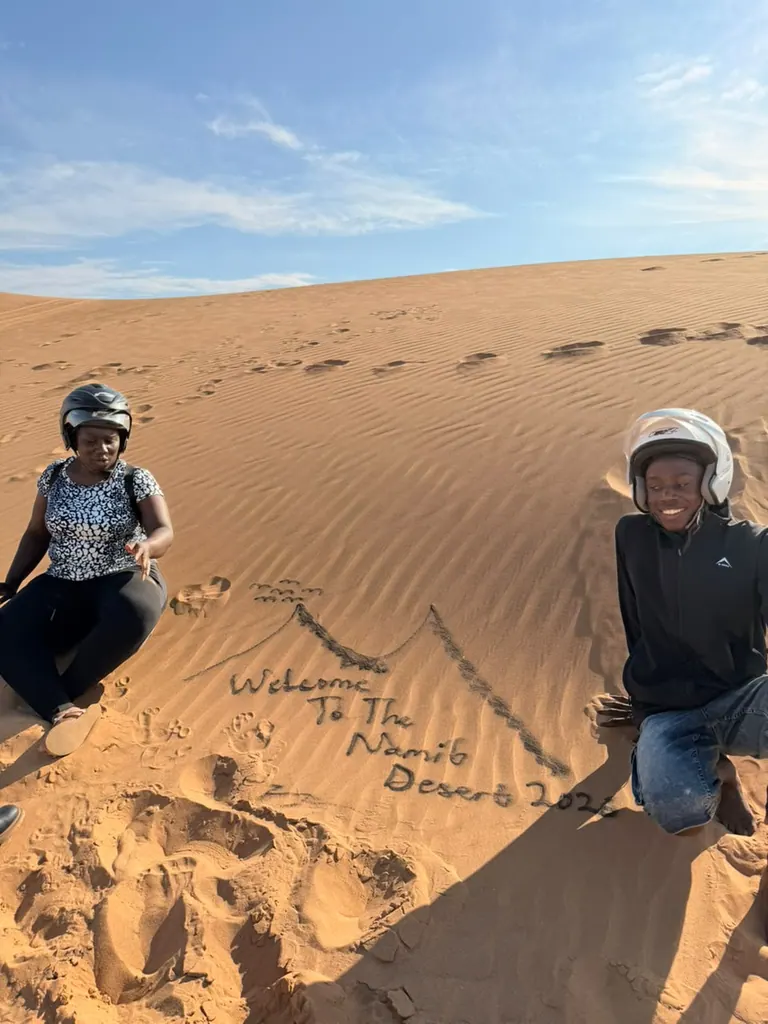 Two travellers sitting in the dunes beside a message written in the sand