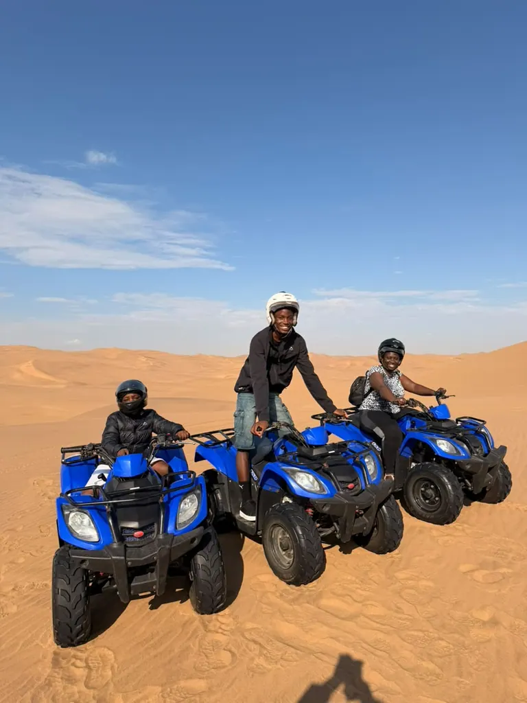Three travellers sitting on blue quad bikes in the dunes