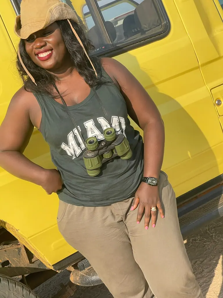 Irene smiling in a safari hat with binoculars beside a yellow vehicle