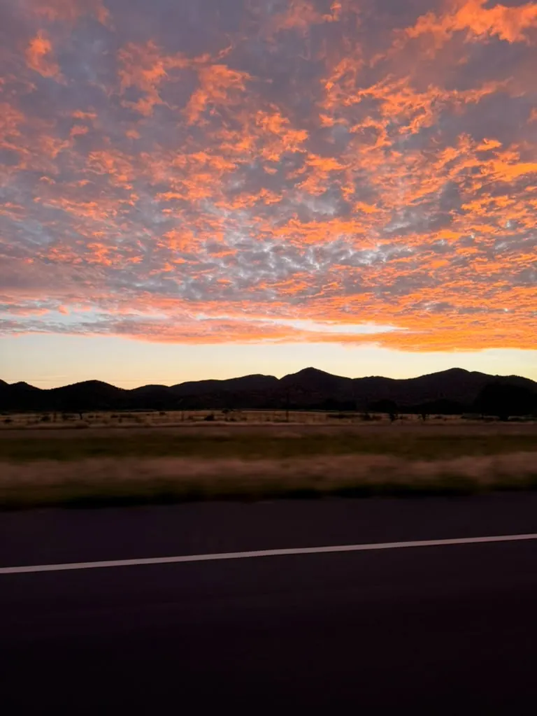 Orange sunset clouds above a mountain silhouette and a road